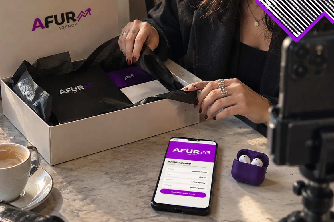 Kafedə qadın AFUR loqolu PR qutusunu açır, ştativdəki telefon onu çəkir; masadakı telefonda elektron vizitka.